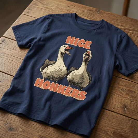 Navy blue Nice Honkers t-shirt laid flat on a wooden table showing the full pair of geese and bold orange text, classic cheeky animal pun tee