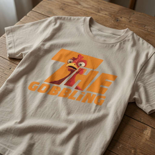 Beige The Gobbling t-shirt laid flat on a wooden surface showing the full turkey graphic, mens fun Christmas pub day turkey statement tee