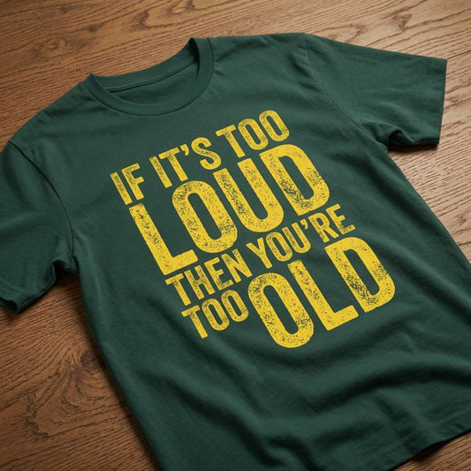 Glazed green If It’s Too Loud Then You’re Too Old t-shirt laid flat on a wooden surface showing the full distressed yellow slogan, funny design that every cheeky lad will claim