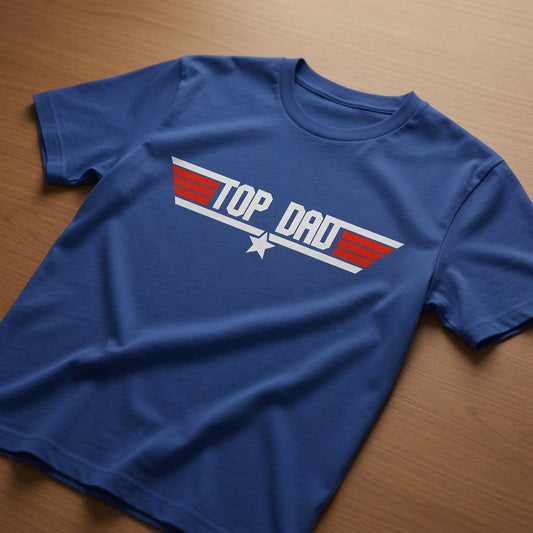 Worker blue Top Dad t-shirt laid flat on a wooden surface with the Top Gun-style logo, fun and witty dad Christmas gift design