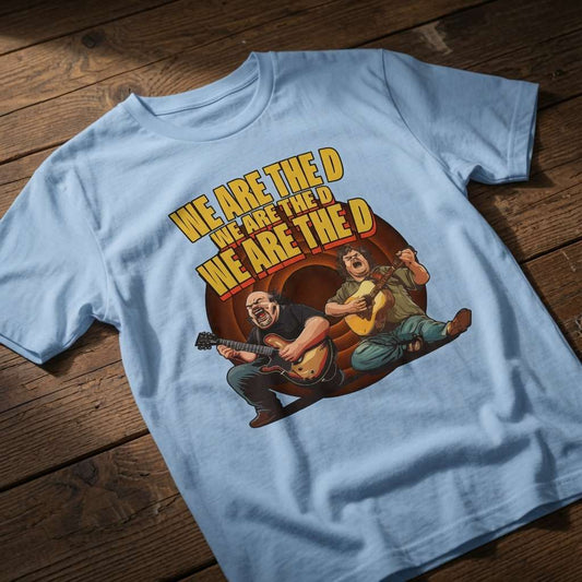 Light blue We Are The D t-shirt laid flat on a wooden surface showing the full Tenacious D parody graphic, blue soul mens music-inspired design that every cheeky lad will claim