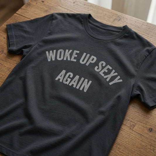 Black Woke Up Sexy Again t-shirt laid flat on a wooden surface showing the arched slogan, funny cheeky ladies slogan shirt full of pure attitude
