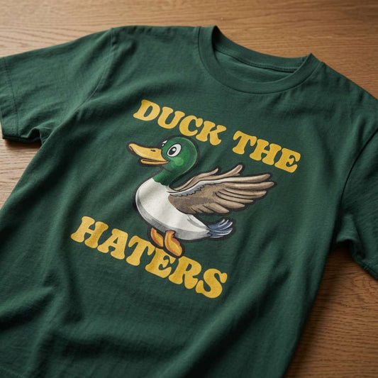 Green Duck The Haters t-shirt laid flat on a wooden surface showing the full cartoon duck graphic, witty mens duck pun graphic shirt full of pure attitude