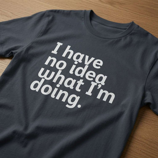 Ink grey I Have No Idea What I’m Doing t-shirt laid flat on a wooden surface showing the full white slogan, witty mens relatable cheeky slogan design full of pure attitude