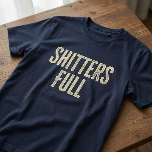 Navy Shitters Full t-shirt laid flat on a wooden surface with bold distressed lettering, witty mens comedy Christmas movie statement design
