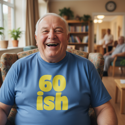 Man wearing a blue t-shirt with '60ish' on it, sitting in a room with other people.
