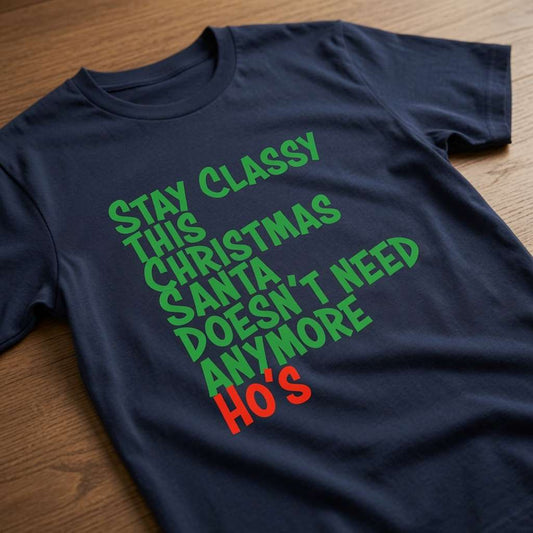 Navy Stay Classy This Christmas Santa Doesn’t Need Anymore Ho’s t-shirt laid flat on a wooden surface showing the full slogan, funny rude ladies Christmas party design full of pure attitude