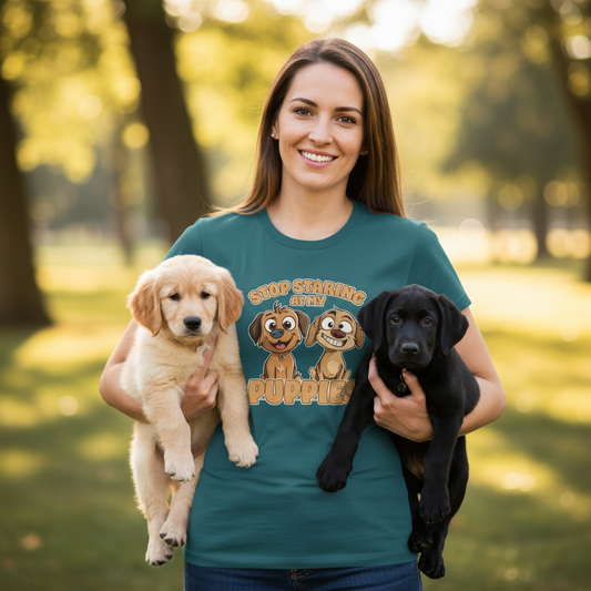 Woman holding two puppies with a shirt featuring cartoon dogs and text in a park setting