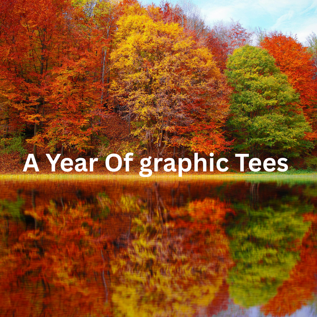 Vibrant autumn trees in red, orange, and green reflect on a calm lake under a blue sky. Bold white text reads, "A Year Of Graphic Tees."