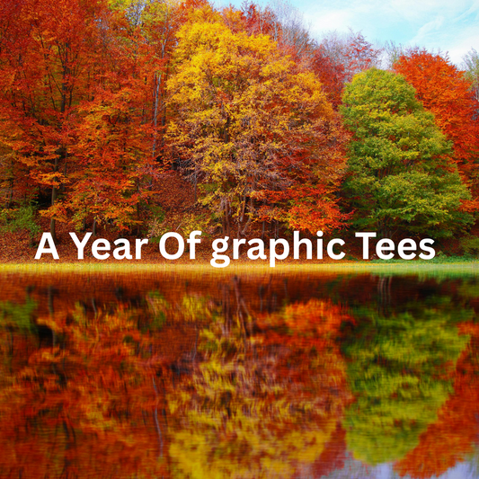 Vibrant autumn trees in red, orange, and green reflect on a calm lake under a blue sky. Bold white text reads, "A Year Of Graphic Tees."