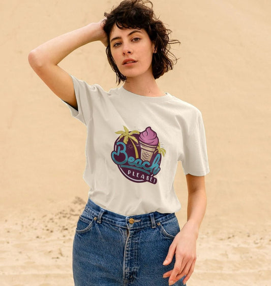 A person stands on a sandy beach wearing a white T-shirt with a colourful design that includes palm trees and an ice cream cone, captioned "Beach Please."