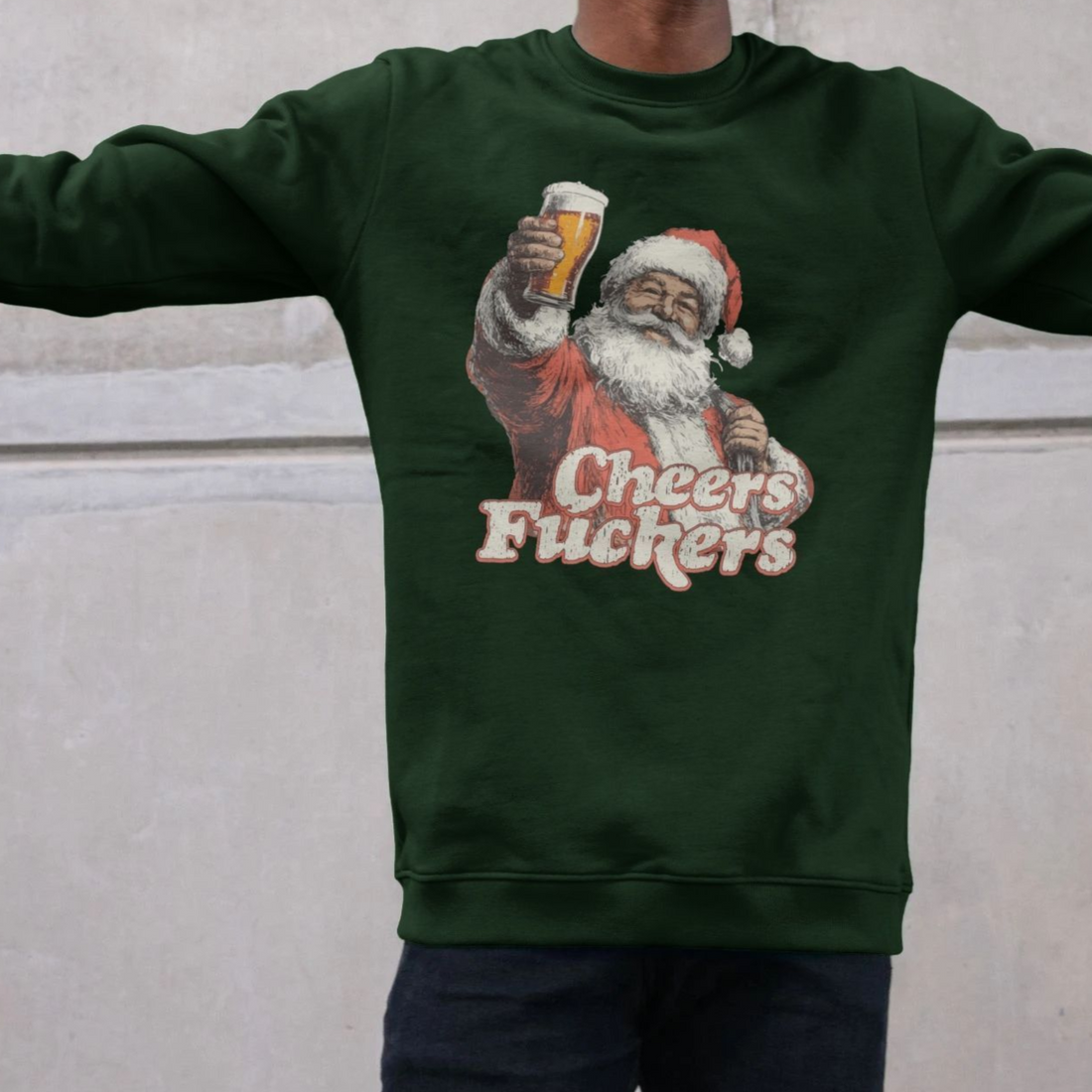 A person wearing a dark green sweatshirt featuring a vintage-style Santa holding a beer and the text "Cheers Fu**ers," conveying humor and festive irreverence.