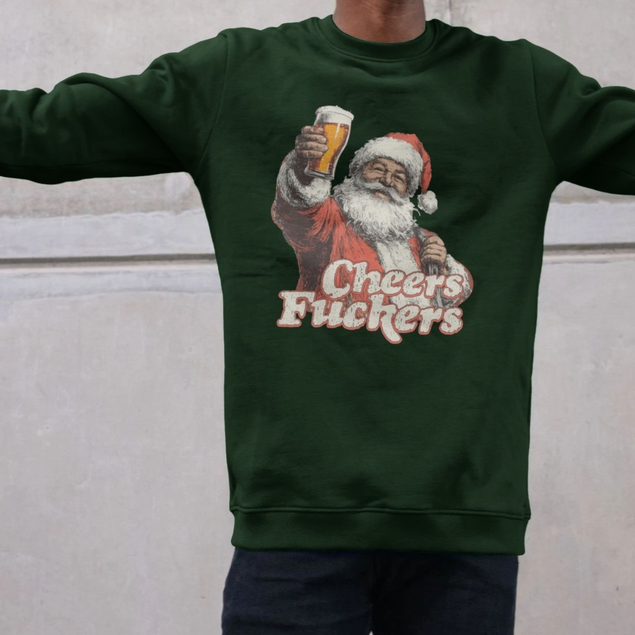 A person wearing a dark green sweatshirt featuring a vintage-style Santa holding a beer and the text "Cheers Fu**ers," conveying humor and festive irreverence.