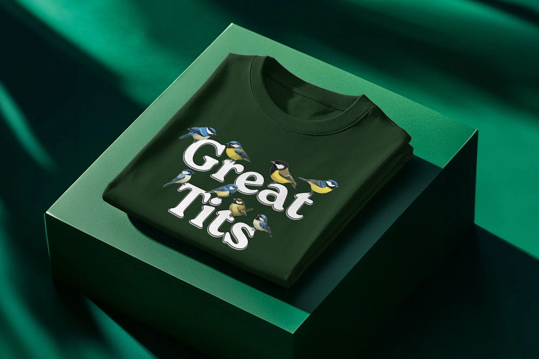 Green shirt featuring illustrated birds and the text "Great Tits," lies folded on a green surface. Bright, playful design with a nature theme.