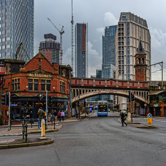 Manchester city centre street scene showing historic architecture blended with modern skyscrapers, a double-decker bus, and urban infrastructure.