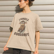 A person in a beige T-shirt with a cartoon bull sitting on a toilet and the text 