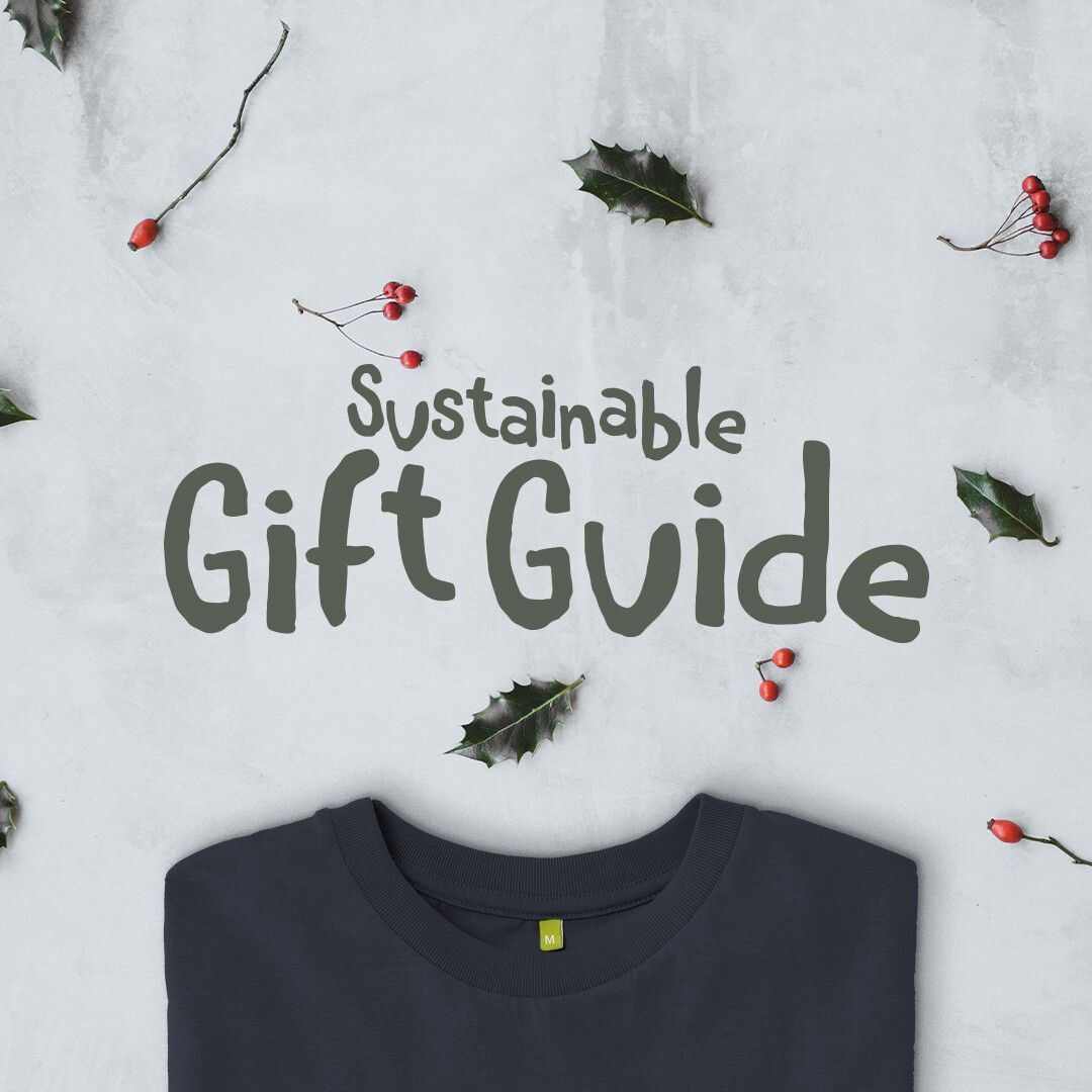Dark text on a light background reads "Sustainable Gift Guide." Surrounding are holly leaves and berries. Below, part of a folded dark shirt is visible.