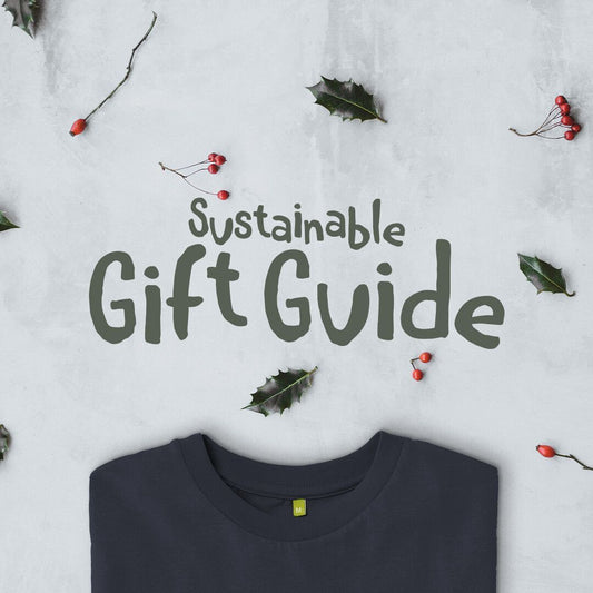 Dark text on a light background reads "Sustainable Gift Guide." Surrounding are holly leaves and berries. Below, part of a folded dark shirt is visible.