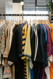 A diverse array of shirts neatly hung on a clothing rack, showcasing various colors and patterns like stripes and paisley, in a well-lit retail setting.