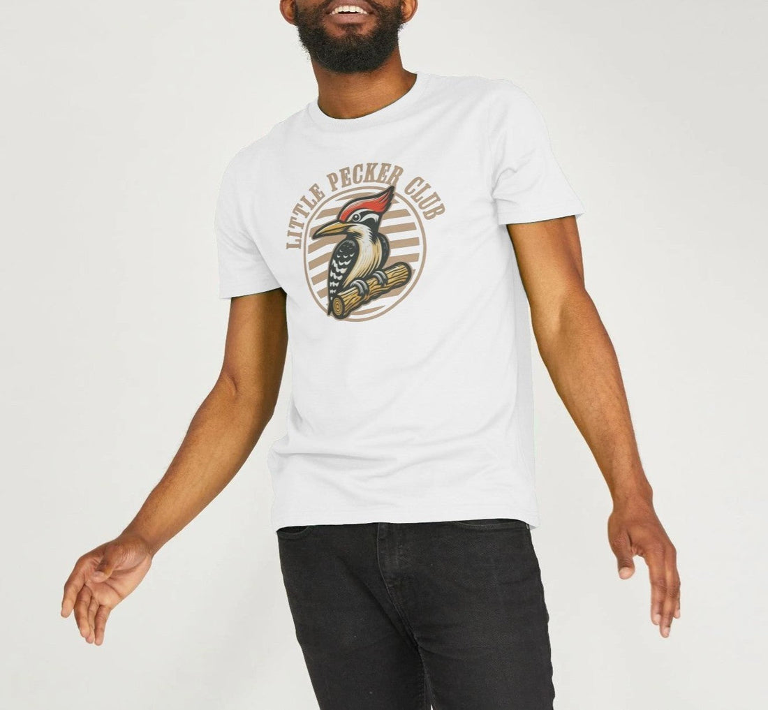 Man in a white "Little Pecker Club" T-shirt featuring a colourful woodpecker graphic. Wearing black jeans, he's mid-motion, smiling energetically.