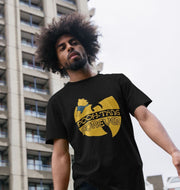 Man with a large afro stands in front of a tall building, wearing a black T-shirt with a playful 