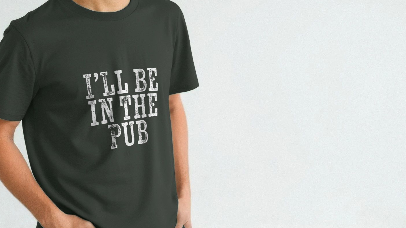 A person wearing a dark dad slogan shirt with bold, white text reading "I'll Be in the Pub," expressing a casual, humorous tone against a light background.