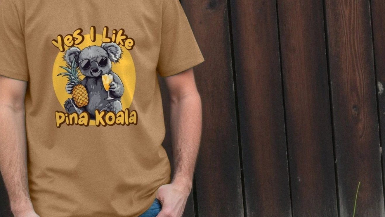 A person wears a funny animal T-shirt with a playful design of a koala in sunglasses holding a pineapple and a drink. Text reads "Yes I Like Pina Koala." The tone is humorous.