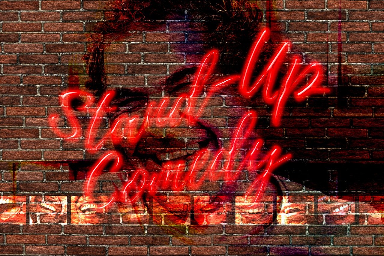 Neon red "Stand-Up Comedy" text glows over a brick wall backdrop, blending into a subtly smiling face, creating a lively and humorous atmosphere.