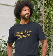 A person with an afro and beard smiles slightly while wearing a navy t-shirt featuring the phrase 