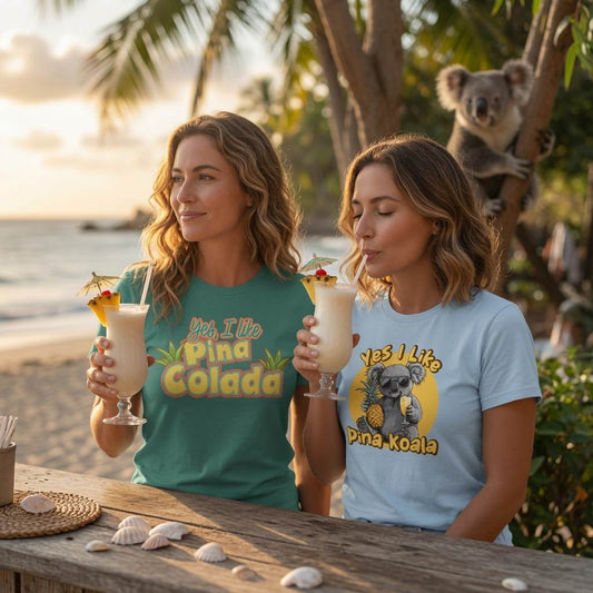 Two women drinking piña coladas on a tropical beach, wearing Teevolution graphic t-shirts reading "Yes, I Like Pina Colada" and "Yes I Like Pina Koala" with a koala bear looking on.