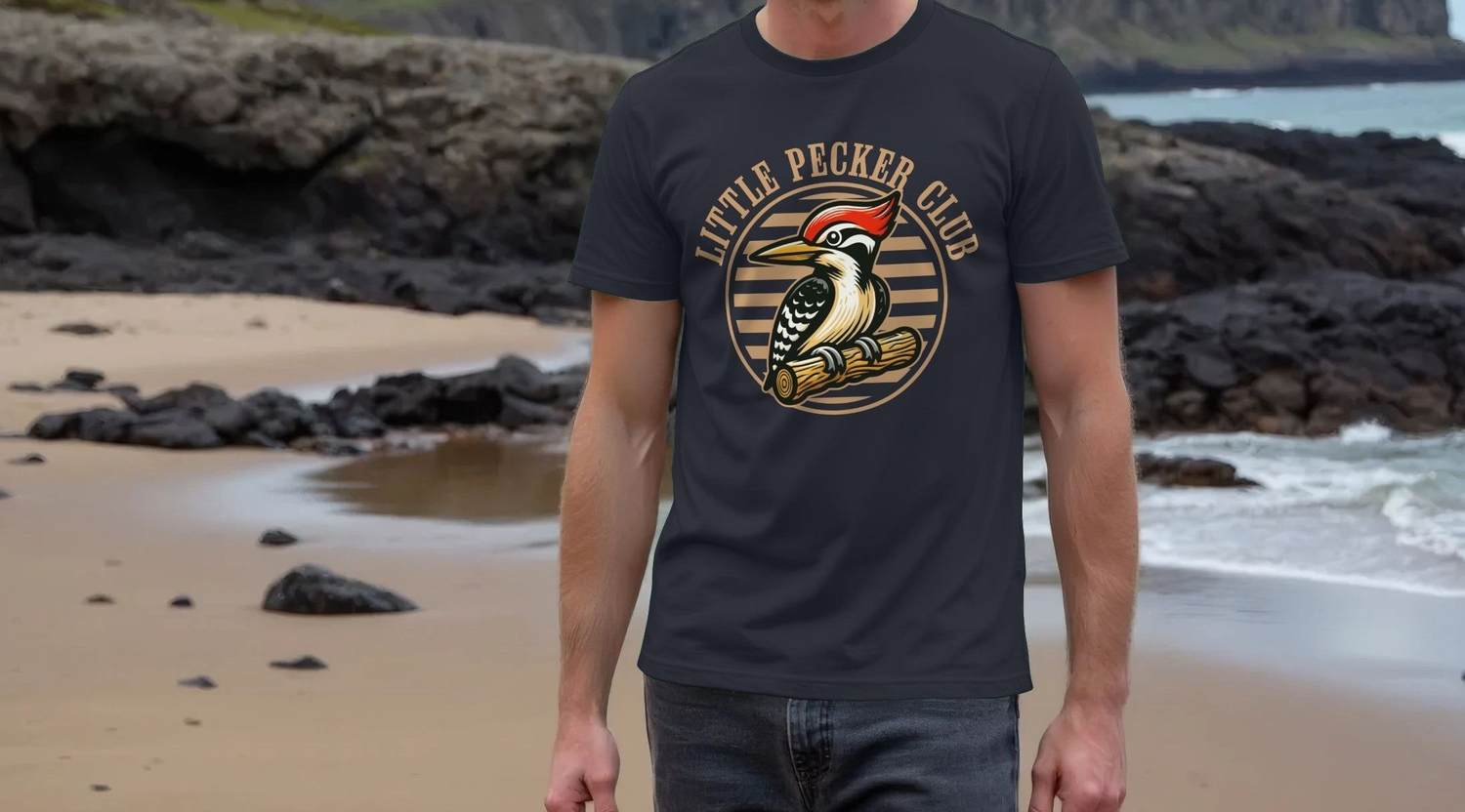 A Man stands on a rocky beach wearing a Stag Do T-shirt with a woodpecker logo and the text "Little Pecker Club." The background shows waves and cliffs.