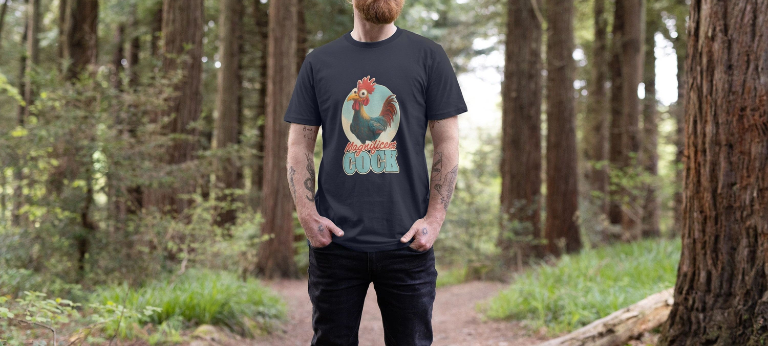 Man standing on a forest path wearing a black Rude Mens T-shirt with a colorful rooster and playful text, conveying a casual and humorous mood.