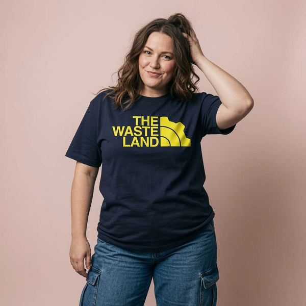Woman with one hand in her hair while wearing a navy The Wasteland t-shirt with a North Face-style gear logo, vault tee