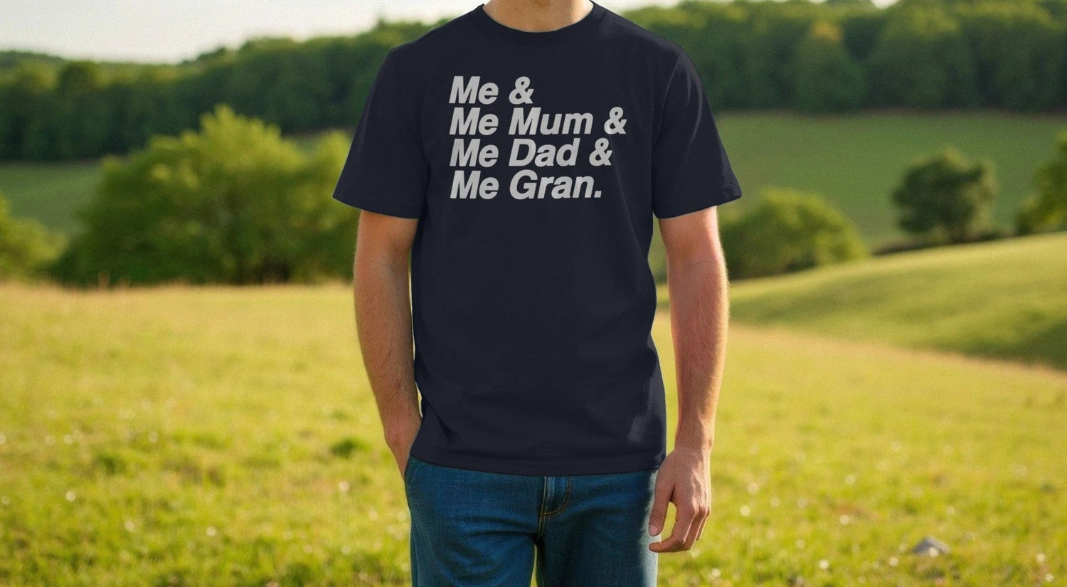 Man in a black Football T-shirt with text "Me & Me Mum & Me Dad & Me Gran," stands in a sunny, lush green field. Casual, serene outdoor setting.