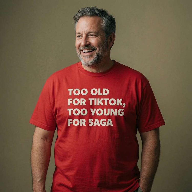 Bearded man smiling and looking slightly to the side while wearing a red Too Old For TikTok, Too Young For Saga t-shirt, humorous age-related slogan that hits the middle-aged sweet spot