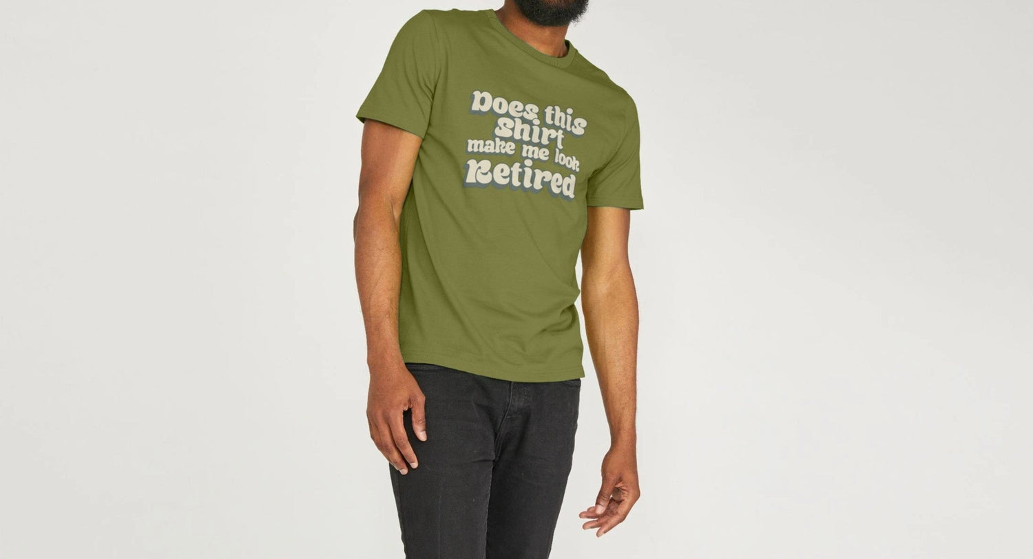 A smiling man in a green Retirement T-shirt with the text "Does this shirt make me look retired?" stands casually against a light gray background. Playful tone.