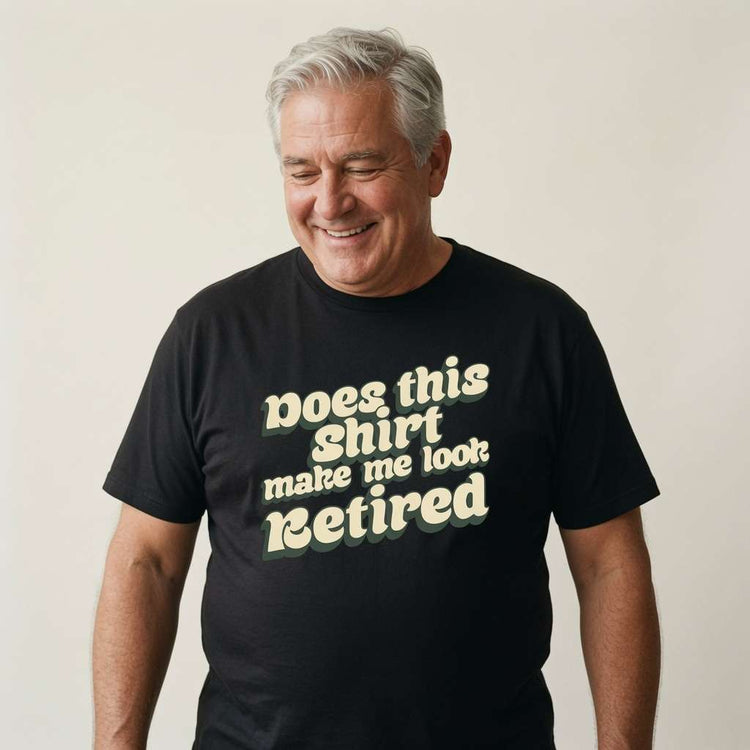 Grey-haired man smiling looking down in black Does This Shirt Make Me Look Retired tee, cheeky fun retirement slogan