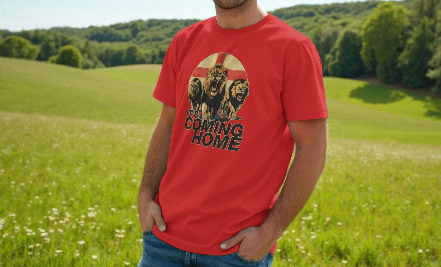 Man in red "It's Coming Home" England t-shirt with lion graphic, standing in a lush, green park. Grass and trees under a clear sky convey tranquility.