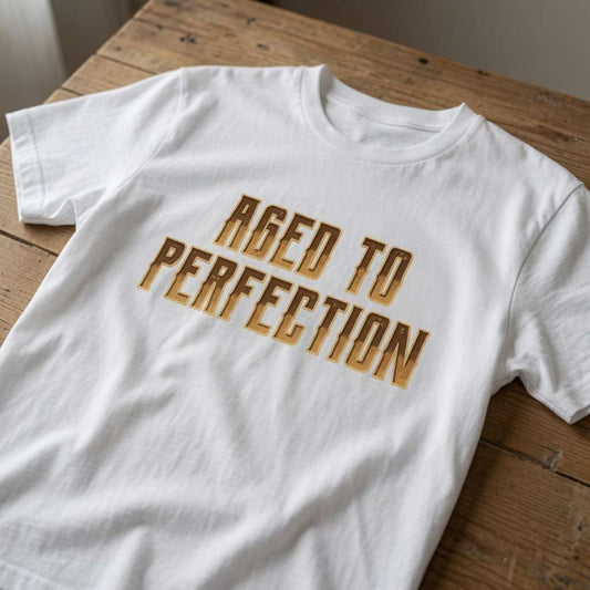 White Aged To Perfection slogan t-shirt on rustic wooden table, funny age-related gift for the refined legend