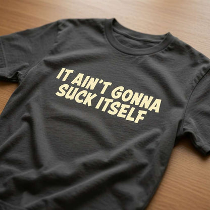 Khaki It Ain’t Gonna Suck Itself t-shirt laid flat on a wooden surface showing the full slogan, funny rude banter slogan design full of pure attitude