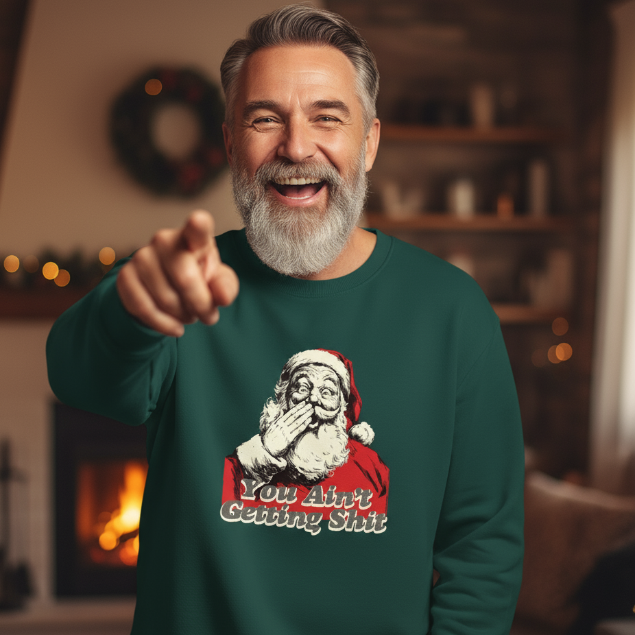 Man wearing a green rude Christmas sweatshirt with a humorous Santa Claus graphic, pointing forward in a cozy room.