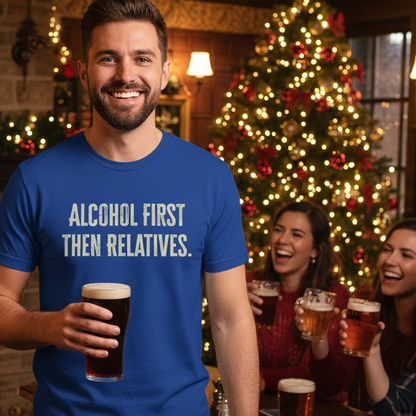 Man wearing a blue Beer slogan t-shirt with 'Alcohol First Then Relatives' text, holding a beer, with people and a Christmas tree in the background.