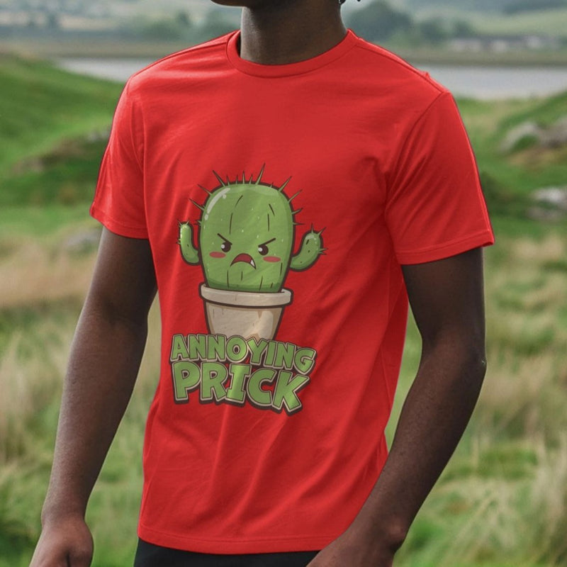Man wearing a red funny graphic T-shirt with an angry cartoon cactus and the phrase "Annoying Prick." The background is a grassy landscape with hills.