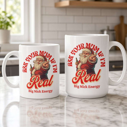 Two white mugs on a bright kitchen counter feature a cheerful vintage Santa and red lettering: “Ask your mum if I’m real” and “Big Nick Energy.”