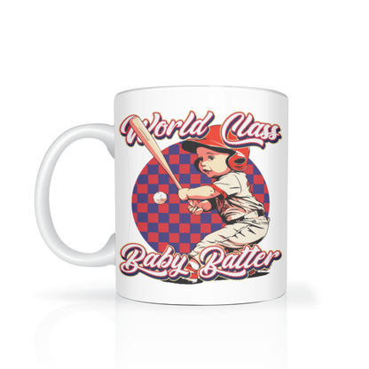White ceramic mug featuring a vintage-style illustration of a young baseball batter swinging, with red-and-blue checkerboard art and “World Class Baby Batter” lettering.