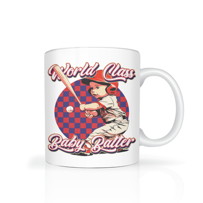 White ceramic mug featuring a vintage illustration of a young baseball player swinging a bat against a red-and-blue checkerboard, with “World Class Baby Batter” text; playful, nostalgic tone.