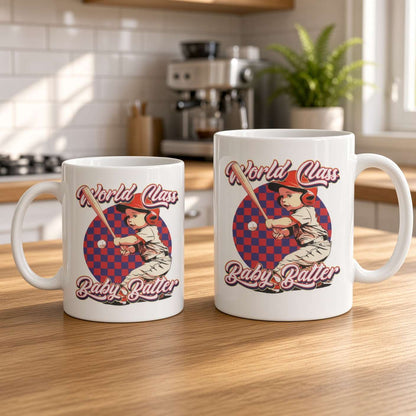 Two white ceramic mugs on a sunlit wooden kitchen counter feature matching retro “World Class Baby Batter” baseball-player designs, creating a warm, playful feel.