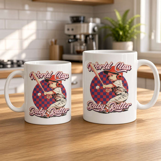 Two white ceramic mugs on a sunlit wooden kitchen counter feature matching retro “World Class Baby Batter” baseball-player designs, creating a warm, playful feel.