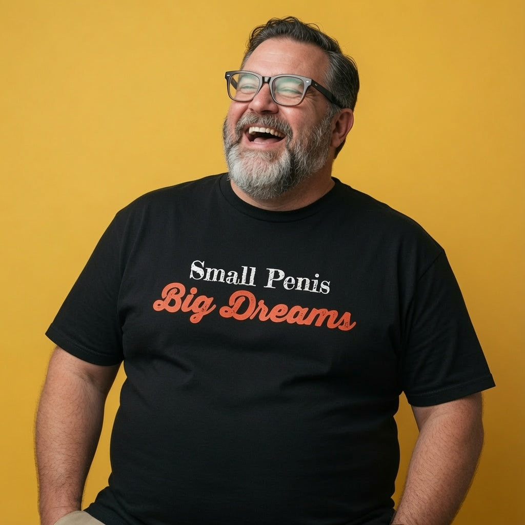 Man laughing while wearing a black Small Penis Big Dreams t-shirt, funny mens offensive rude slogan design that every cheeky lad will claim