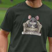 Green animal t-shirt with a animal graphic of a Chinchilla sitting on a chair and 'Just chinchillin' slogan, worn by a person.
